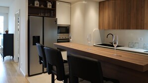 A modern kitchen with a central island, black chairs, a refrigerator, microwave, oven, and wooden cabinets. - Résidence Ciomal by Interhome (Geneva)
