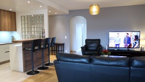 A modern living room with a black leather sofa, a dining area with a bar, and a television displaying a show. - Résidence Ciomal by Interhome (Geneva)
