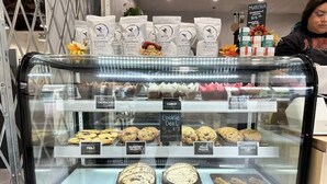Una vitrina de pastelería con diversas opciones de panadería, como galletas y pasteles, y sacos de café al fondo.