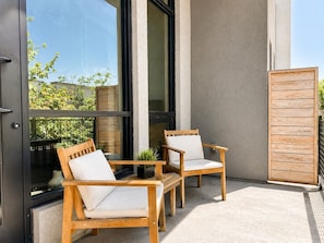 Ein Balkon mit zwei Holzstühlen, einem kleinen Tisch, einem Holzzaun und einem Gebäude mit großen Fenstern.