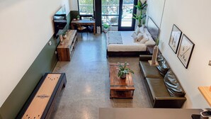Amplia sala de estar con una cama grande, una mesa de centro de madera, un sofá y un escritorio con una silla. Hay plantas en macetas y cuadros en las paredes.