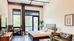 Un dormitorio moderno con cama, escritorio, sofá y ventanas amplias.