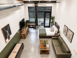 A modern living room with a bed, sofa, and coffee table, featuring a large window and a ceiling fan. - Dog Friendly DTSA Loft 5 Miles to Disney w/ Gym (Santa Ana)