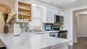 A modern kitchen with white cabinetry, a marble countertop, and a built-in microwave. - Comfy, Convenient, and Charm 3BR Retreat near BGSU (Bowling Green)
