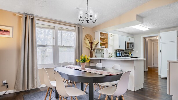 A modern kitchen with white cabinets, a microwave, and a dining area with a round table and white chairs. - Comfy, Convenient, and Charm 3BR Retreat near BGSU (Bowling Green)