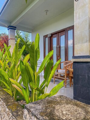 A covered outdoor area with a wooden chair and a table, surrounded by large green plants. - Gapul pinpilinPauxa (Penida Island)