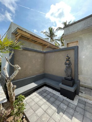 A corner of a building with a concrete wall, a statue, and a small garden area with pebbles and plants. - Gapul pinpilinPauxa (Penida Island)