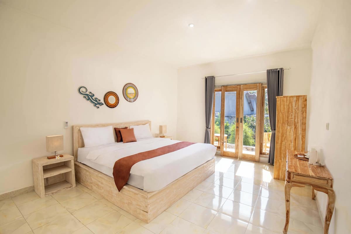 Un dormitorio amplio con una cama grande, una mesita de noche de madera, un escritorio y vistas al exterior a través de un ventanal.