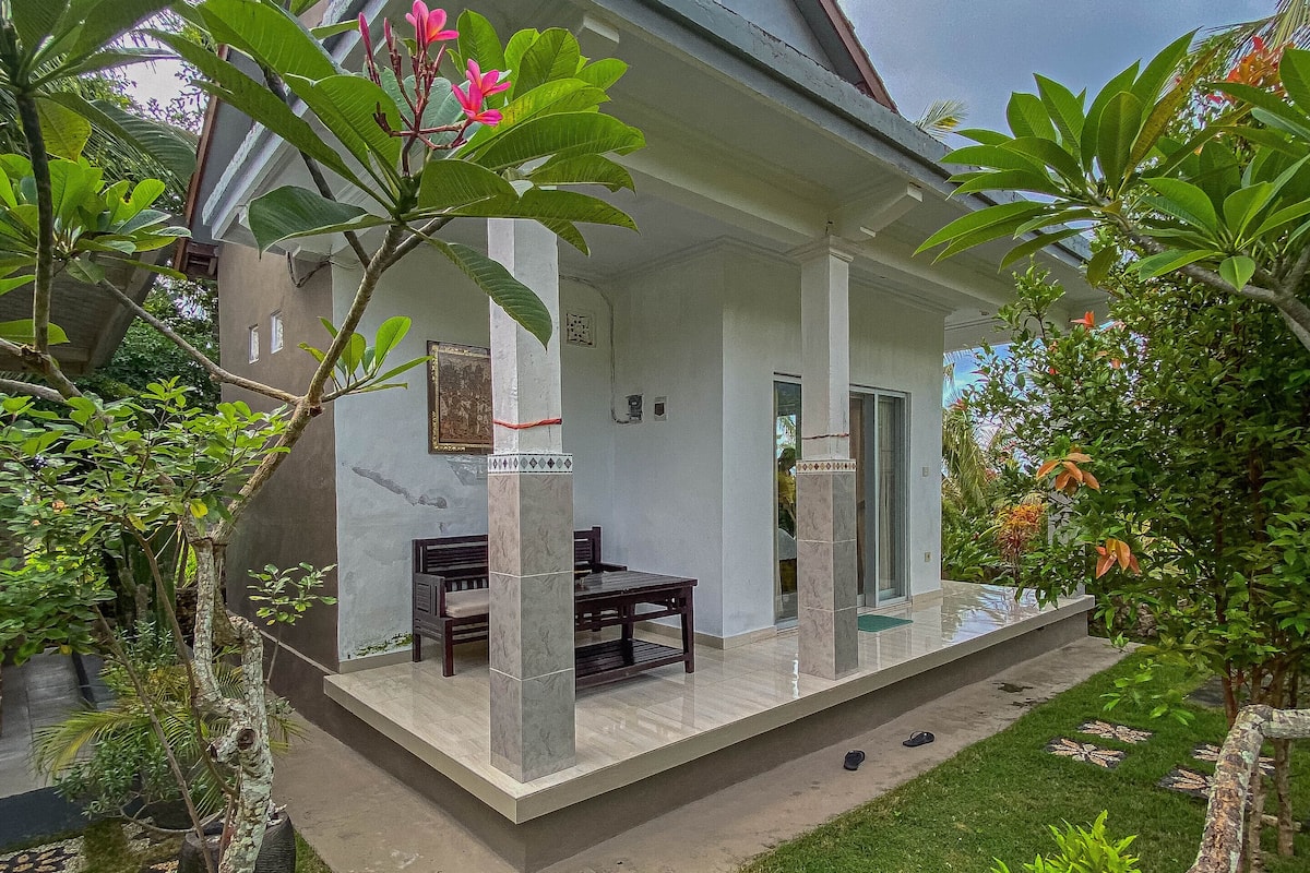 Una casa con porche cubierto, comedor y jardín con diversas plantas.