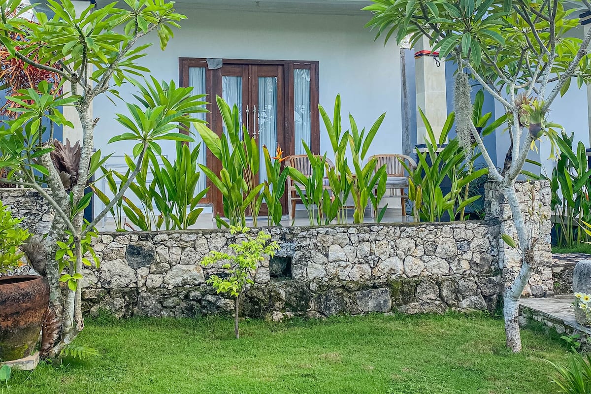 Una casa con un muro de piedra, una puerta de madera y un jardín con diversas plantas.