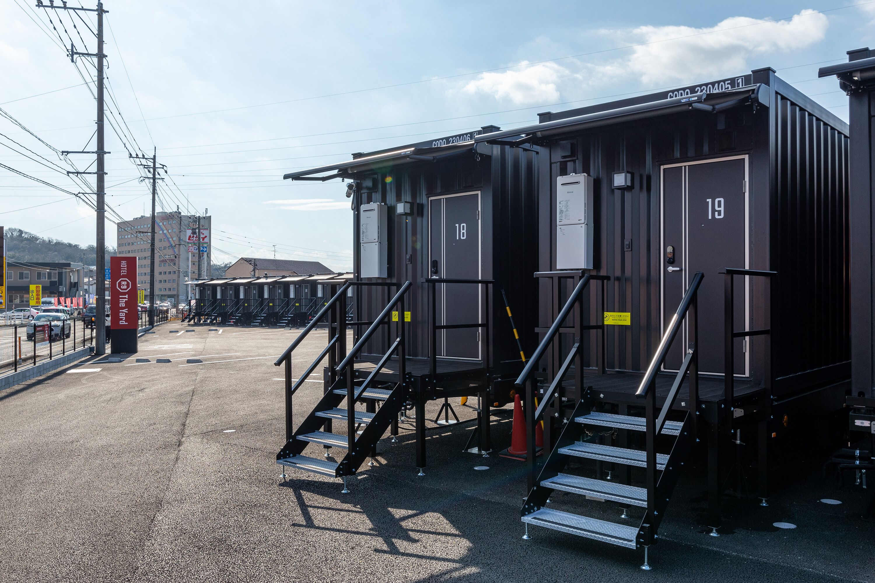 A row of industrial-style buildings with numbered doors, staircases, and a clear sky.