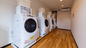 A row of white front-loading washing machines with baskets on top, in a hallway with wooden flooring and white walls. - HOTEL R9 The Yard Arao (Arao)