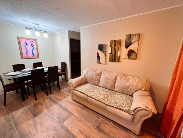 A living room with a beige sofa, a dining table with chairs, and artwork on the walls. - Hermoso y Acogedor Apartamento en el Tabo, Tranquilo y Agradable (El Tabo)