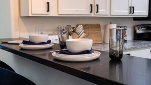 A kitchen counter with two white bowls on plates, a glass, and a wooden cutting board. - Monte Horizon Oasis by HomeSlice Stays (Phoenix)