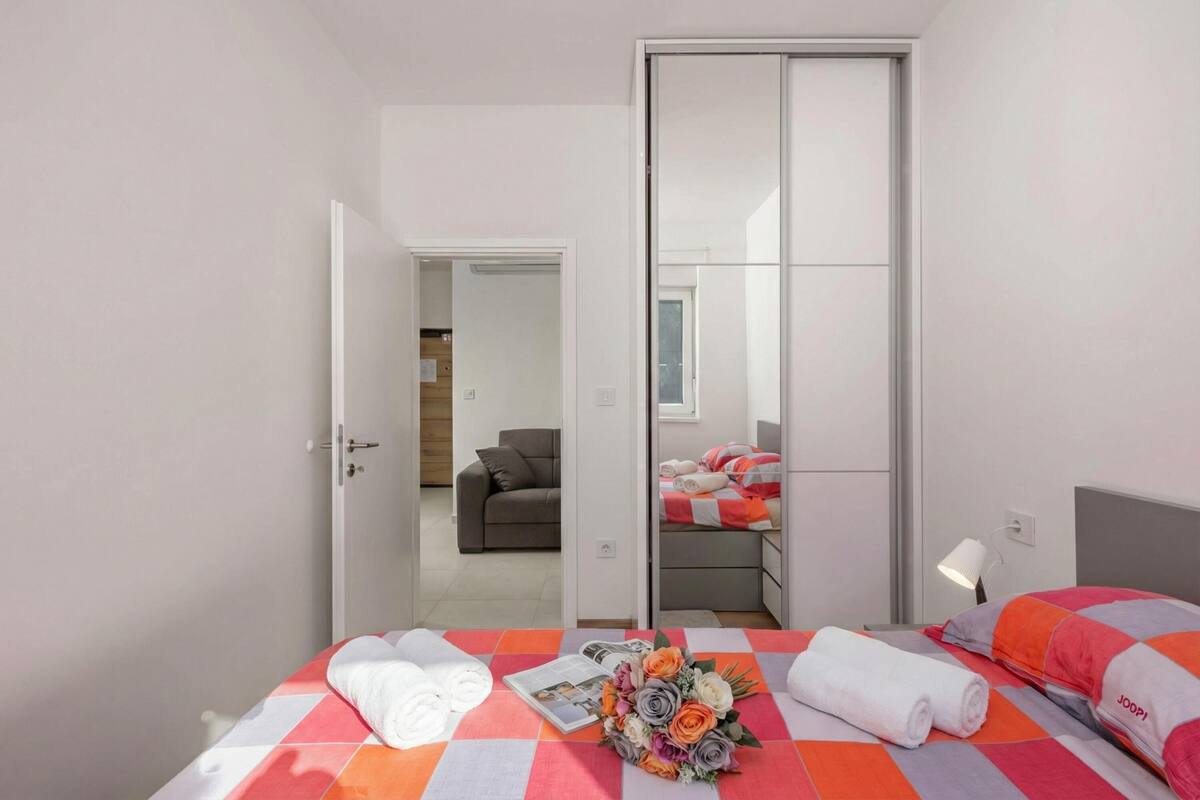 A hotel room with a bed, a nightstand, a lamp, a mirror, and a sliding door leading to another room.