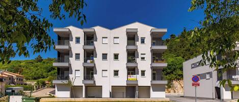 Un immeuble résidentiel à plusieurs étages, doté de balcons, d’un espace de stationnement et d’un panneau indiquant qu’il est interdit de se garer.
