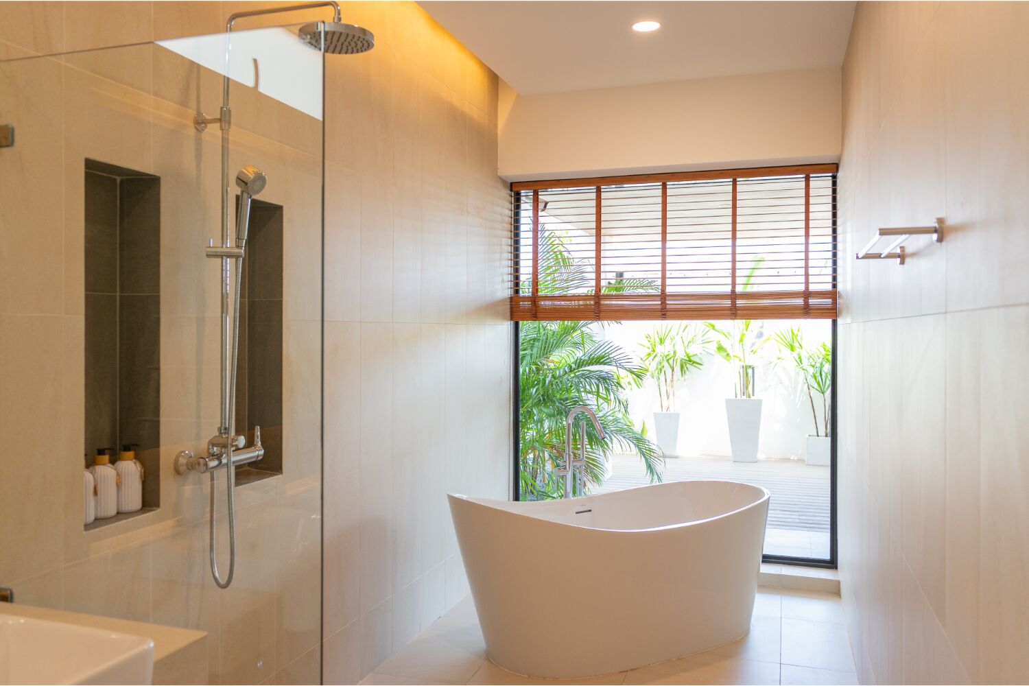 A modern bathroom with a freestanding bathtub, a walk-in shower, and a large window with blinds.