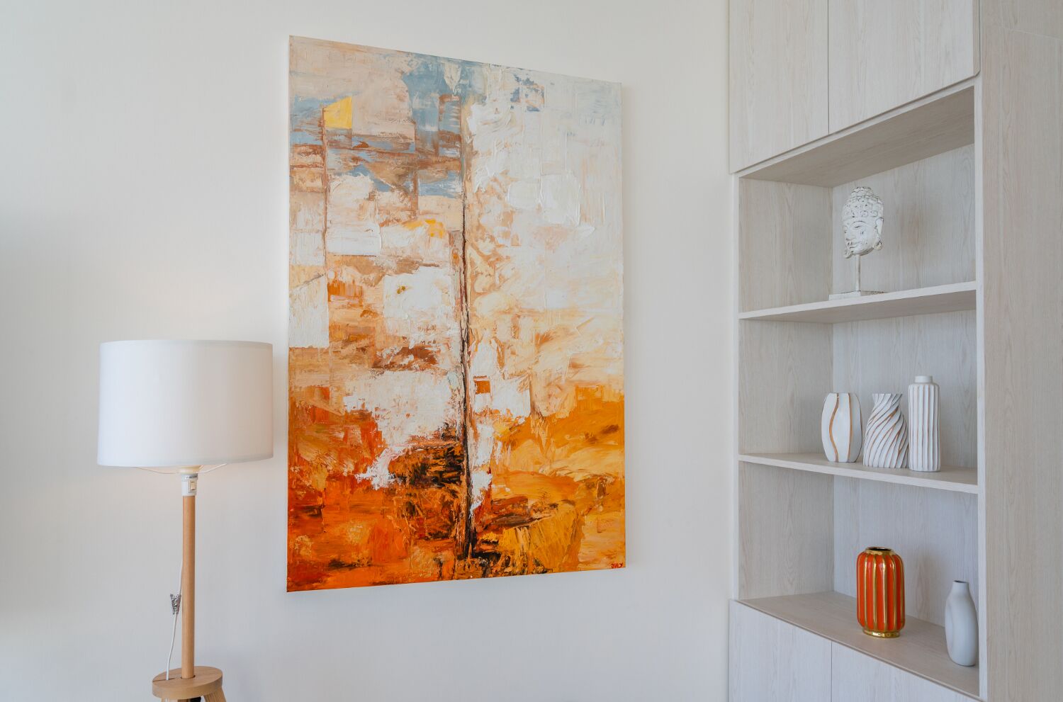 A room with a large abstract painting on the wall, a floor lamp, and a shelving unit with decorative items.