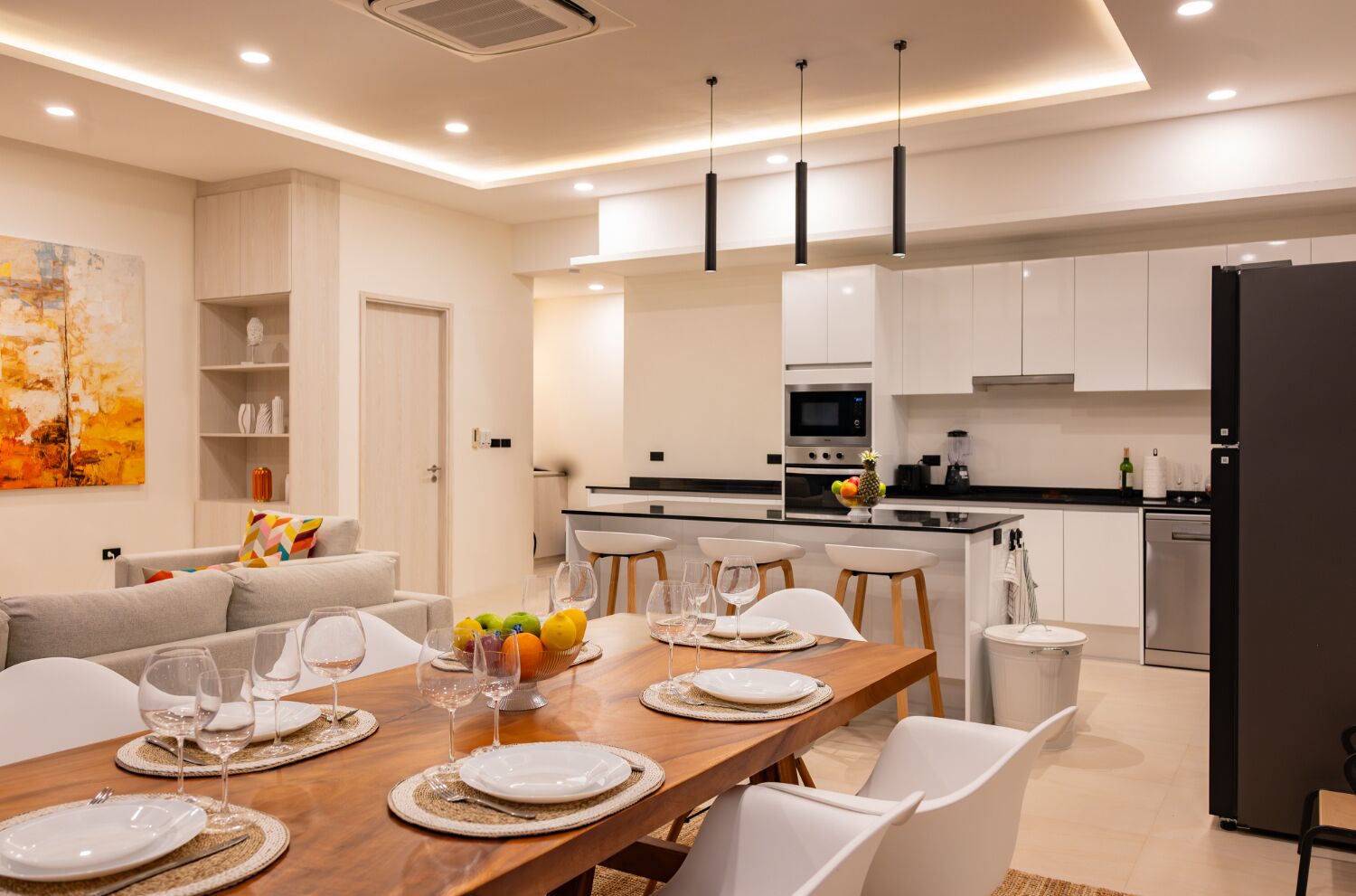 A modern kitchen with white cabinets, a black refrigerator, and a dining area with a wooden table set for four.