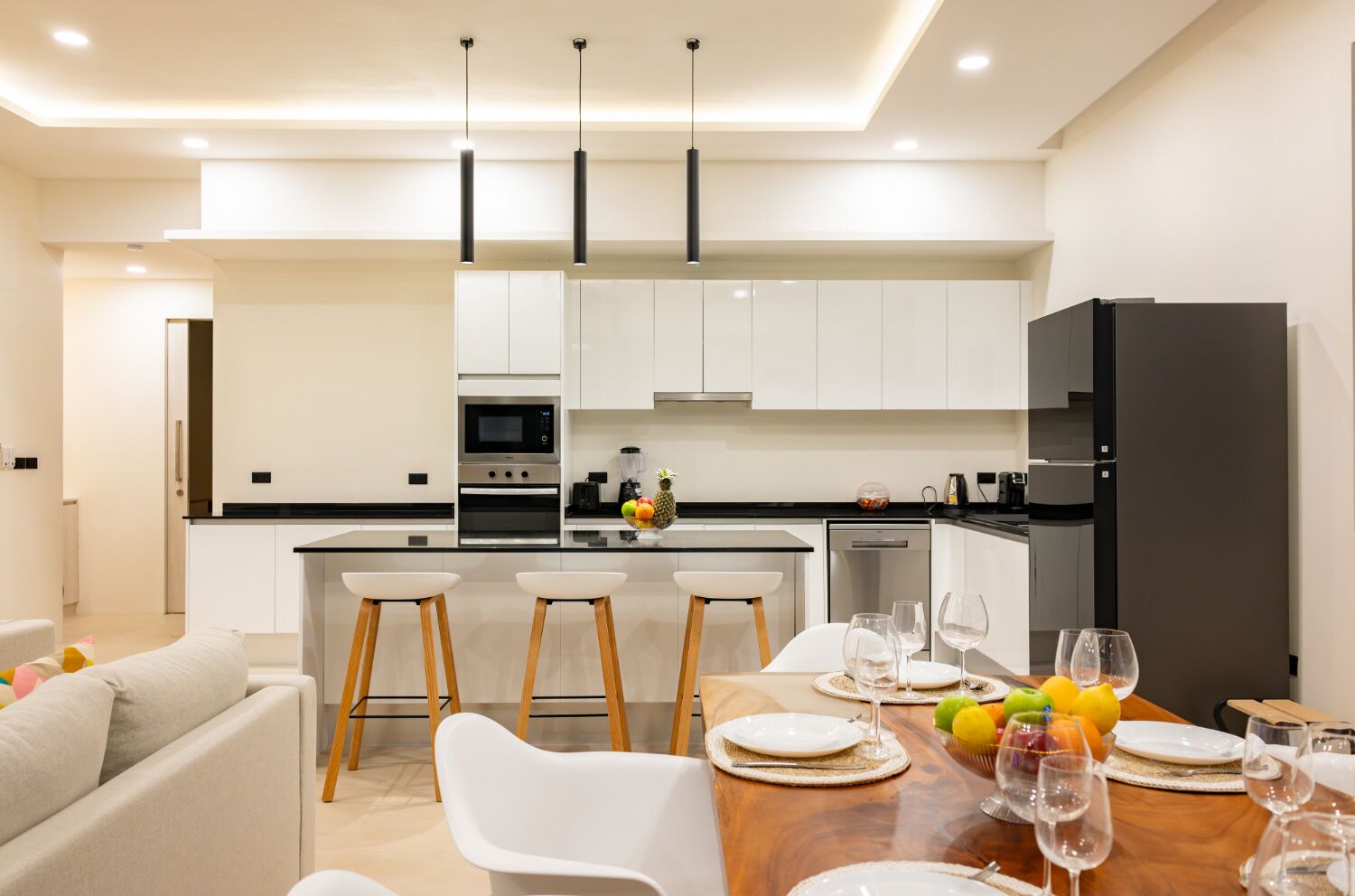 A modern kitchen with white cabinets, a central island with bar stools, and a dining area set for four with a wooden table and white chairs.