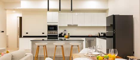 A modern kitchen with white cabinets, a central island with bar stools, and a dining area set for four with a wooden table and white chairs.