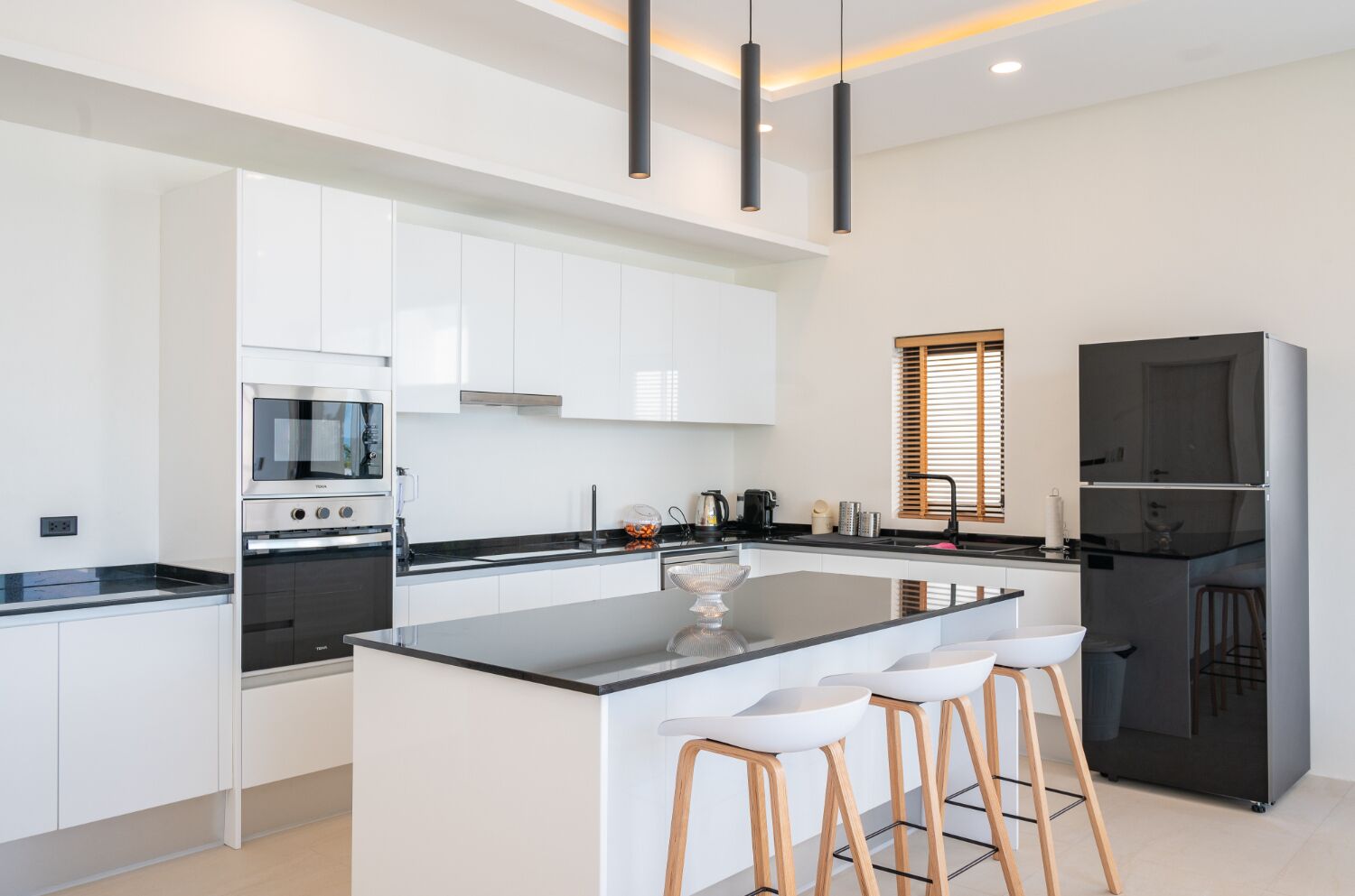 Une cuisine moderne avec des meubles blancs, un îlot central doté de tabourets, un four encastré et un réfrigérateur.