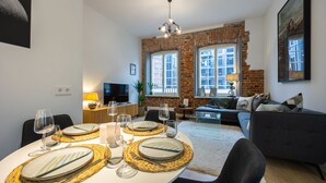 Un coin repas avec une table ronde dressée pour quatre personnes, un mur en briques et un canapé en arrière-plan.