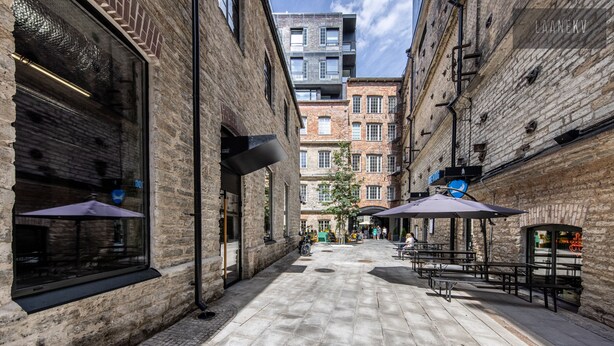 Une rue étroite en milieu urbain, bordée d’immeubles en briques, avec des terrasses et un ciel dégagé.