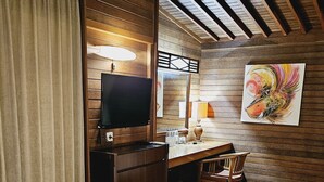 A wooden-paneled room with a television, a desk, a chair, and a painting on the wall. - Kencana Garden Lembongan (Lembongan Island)