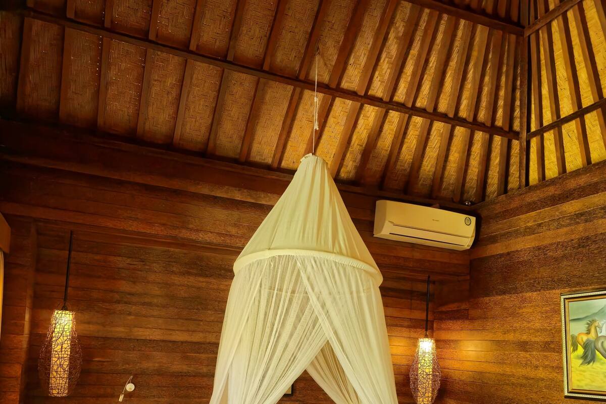Een houten kamer met een bed, een hangend klamboe en een airconditioning.