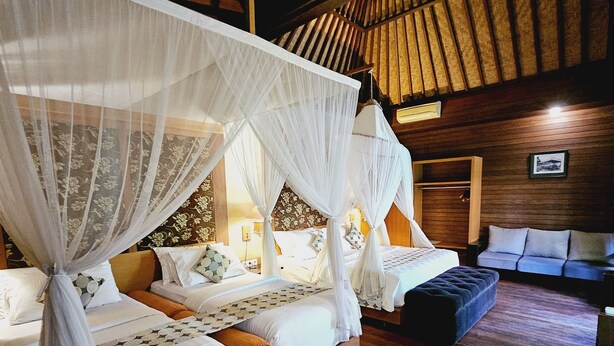 A room with two beds, each with a canopy, wooden flooring, and a sofa. - Kencana Garden Lembongan (Lembongan Island)