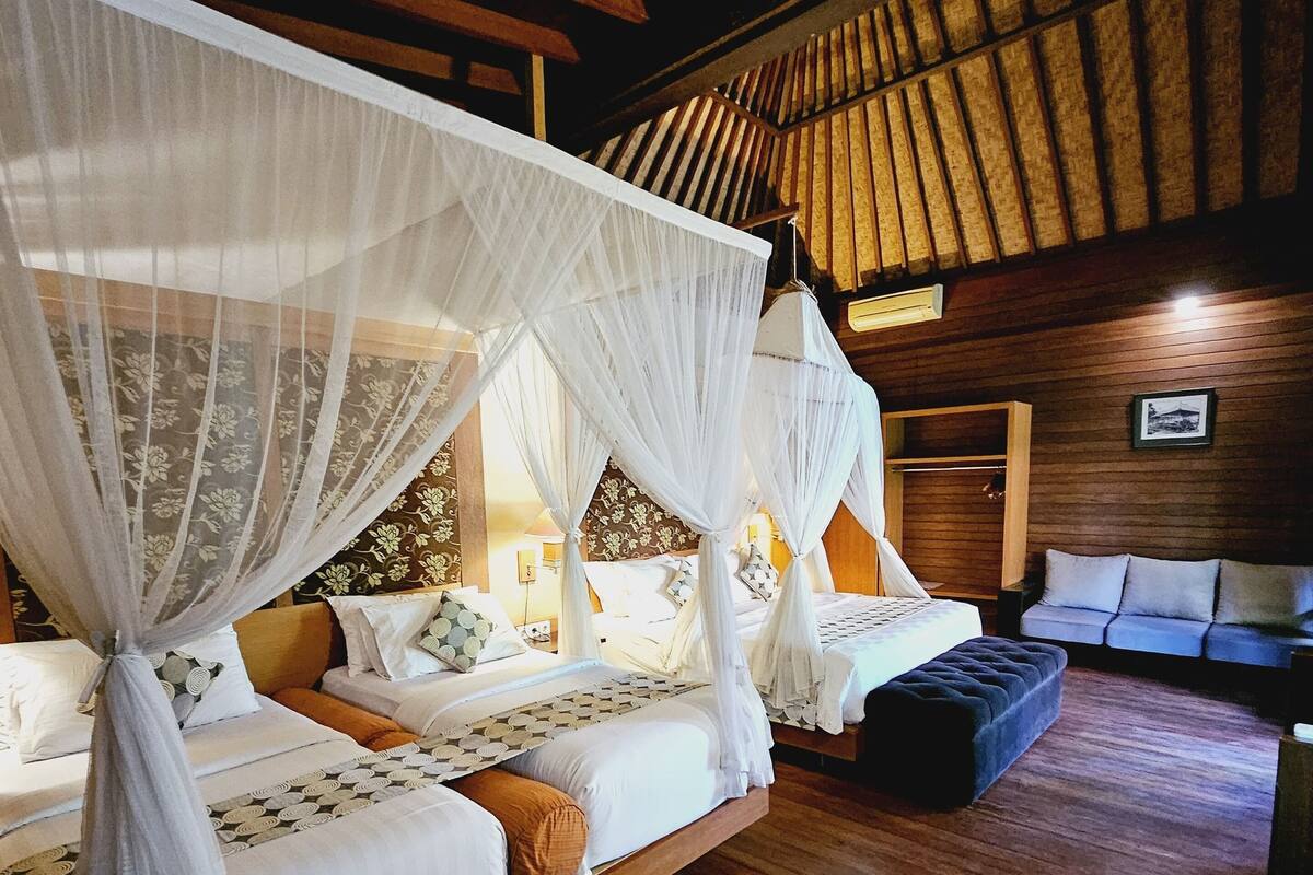 Een kamer met twee bedden, elk met een hemelbed, houten vloeren en een bank.