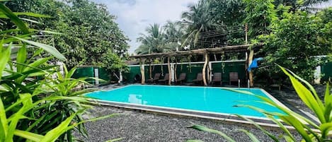 A swimming pool surrounded by lush greenery and a covered seating area.