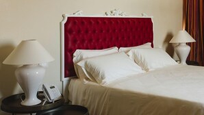 Une chambre d’hôtel avec une tête de lit rembourrée en tissu rouge, du linge de lit blanc, deux tables de chevet avec des lampes et un téléphone sur l’une des tables.