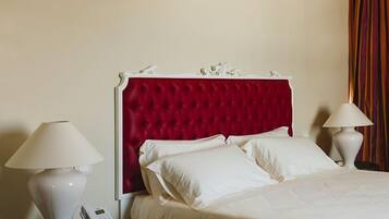 Habitación de hotel con cabecera tapizada en rojo, ropa de cama blanca, dos mesitas de noche con lámparas y un teléfono en una de ellas.