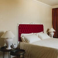 Camera d'albergo con testiera imbottita rossa, biancheria da letto bianca, due comodini con lampade e un telefono su uno dei tavolini.