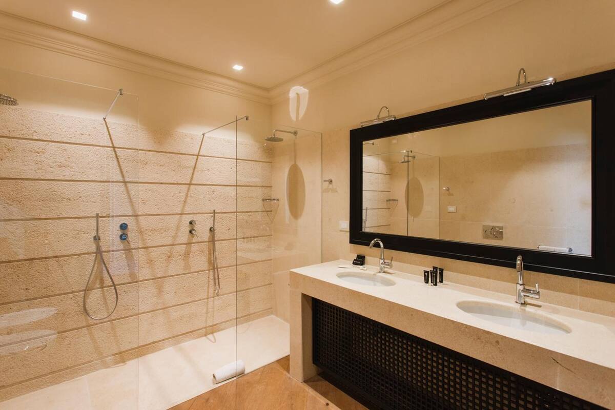 Un baño moderno con ducha acristalada, dos lavabos y un espejo grande.