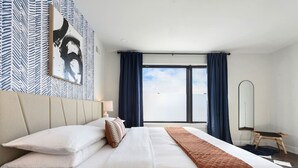 A hotel room with a large bed, a view of the sky, a mirror, and a patterned wall. - ★ HostWise Stays ★ Tech Stay w/ In-Home Cinema & Secure Parking Spot (Pittsburgh)