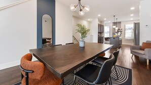 A modern dining area with a dark wooden table, black and orange chairs, a hanging light fixture, and a potted plant. - ★ HostWise Stays ★ Tech Stay w/ In-Home Cinema & Secure Parking Spot (Pittsburgh)