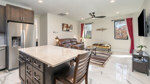 Una cocina moderna con una isla grande, un comedor con mesa de mármol y una sala de estar con sofá y televisor.