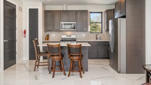 Una cocina moderna con armarios oscuros, un refrigerador de acero inoxidable, un microondas y una estufa. Hay dos taburetes de bar en la isla.