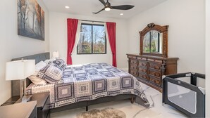 Un dormitorio con cama, cómoda, ventilador de techo y ventana con cortinas.