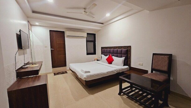 Habitación de hotel con cama, mesita de noche, silla, televisor, armario y ventilador de techo.