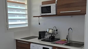 A compact kitchen with a washing machine, a microwave, a sink, and a dish rack. - Hotel Des Roches (Kourou)