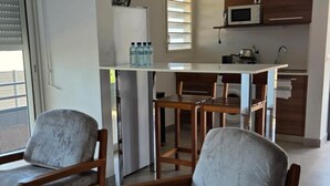 A modern kitchen with a microwave, sink, and bar stools. There are two chairs with cushioned seats. - Hotel Des Roches (Kourou)