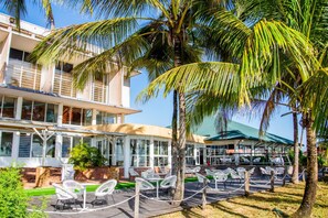Een hotel met terras, palmbomen en een gebouw met grote ramen.