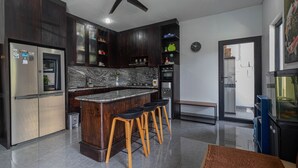 A modern kitchen with dark wood cabinets, a marble countertop, a built-in oven, and a ceiling fan. - Casa Yumi (Denpasar)