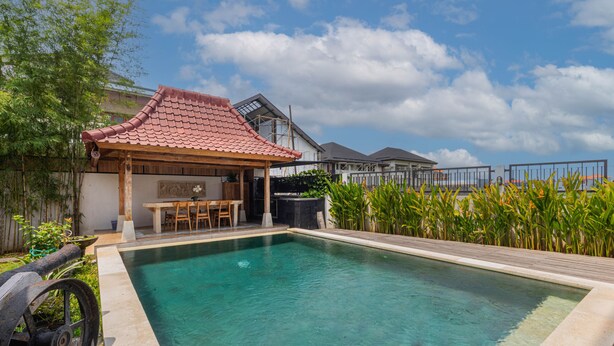 A swimming pool with a wooden deck, a covered seating area, and a view of neighboring houses. - Casa Yumi (Denpasar)