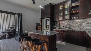 A modern kitchen with dark wood cabinets, a marble countertop, and three black bar stools. - Casa Yumi (Denpasar)