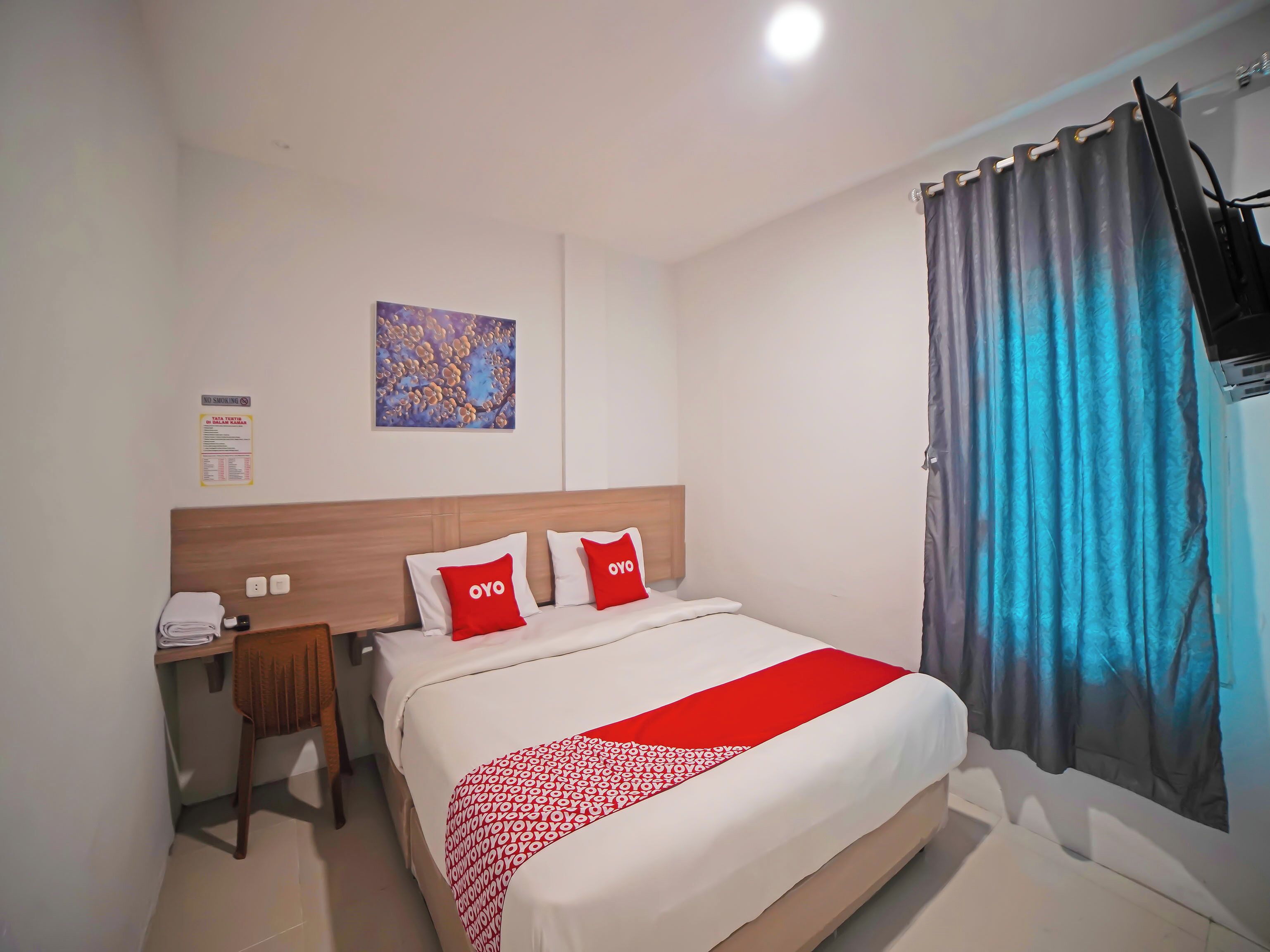 Ein Hotelzimmer mit Bett, Schreibtisch, Stuhl, einem an der Wand befestigten Fernseher und einem Fenster mit Vorhängen.
